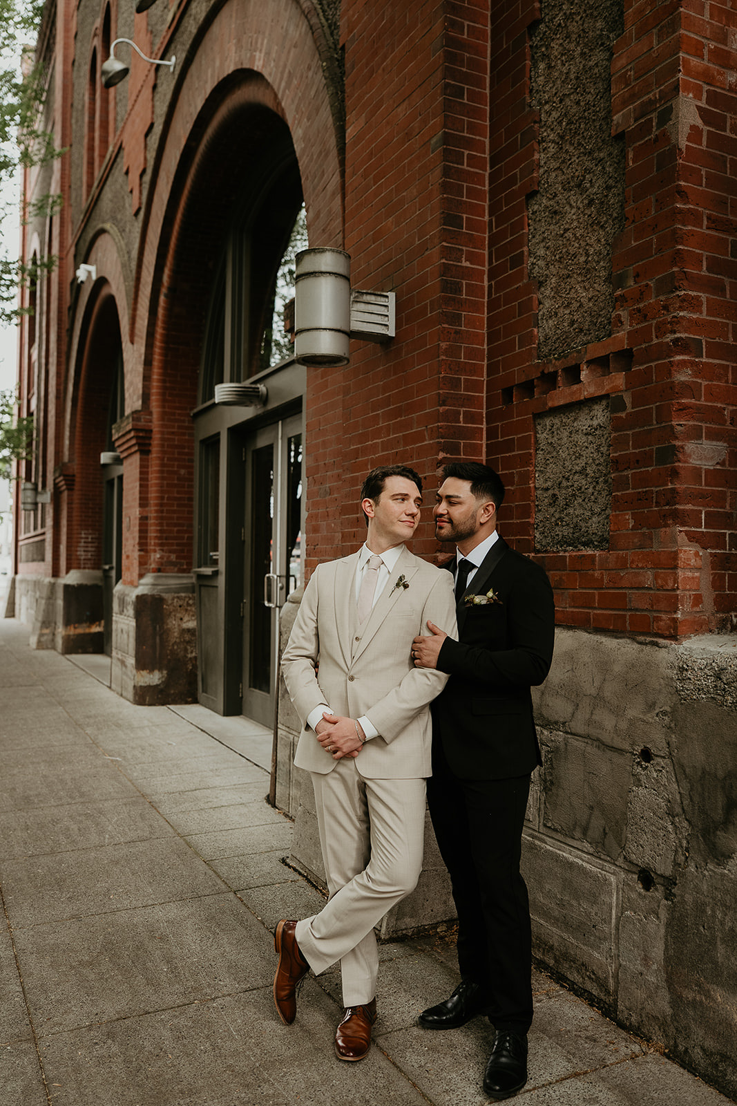Newlyweds holding each other in front of a brick-walled building for an Ecotrust wedding styled shoot.