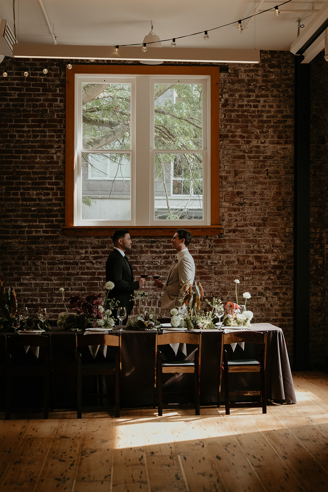 Newlyweds holding wine glasses in front of a fancy wedding table for an Ecotrust wedding styled shoot.