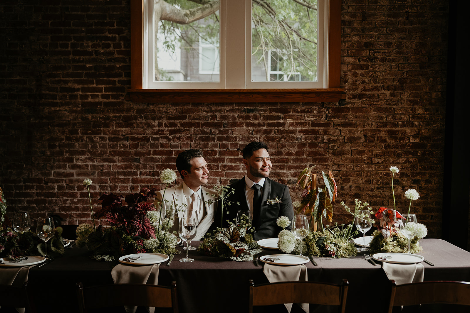 newlyweds sitting at a table arrangement with lots of flowers and table wear for an Ecotrust wedding styled shoot.