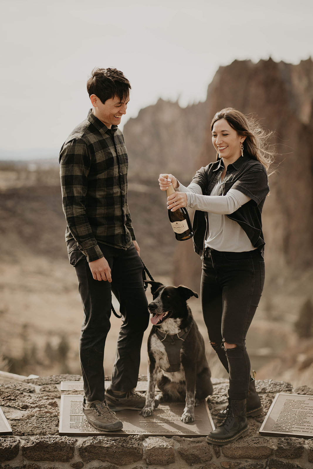 Couple popping champagne bottle at rock climbing engagement session