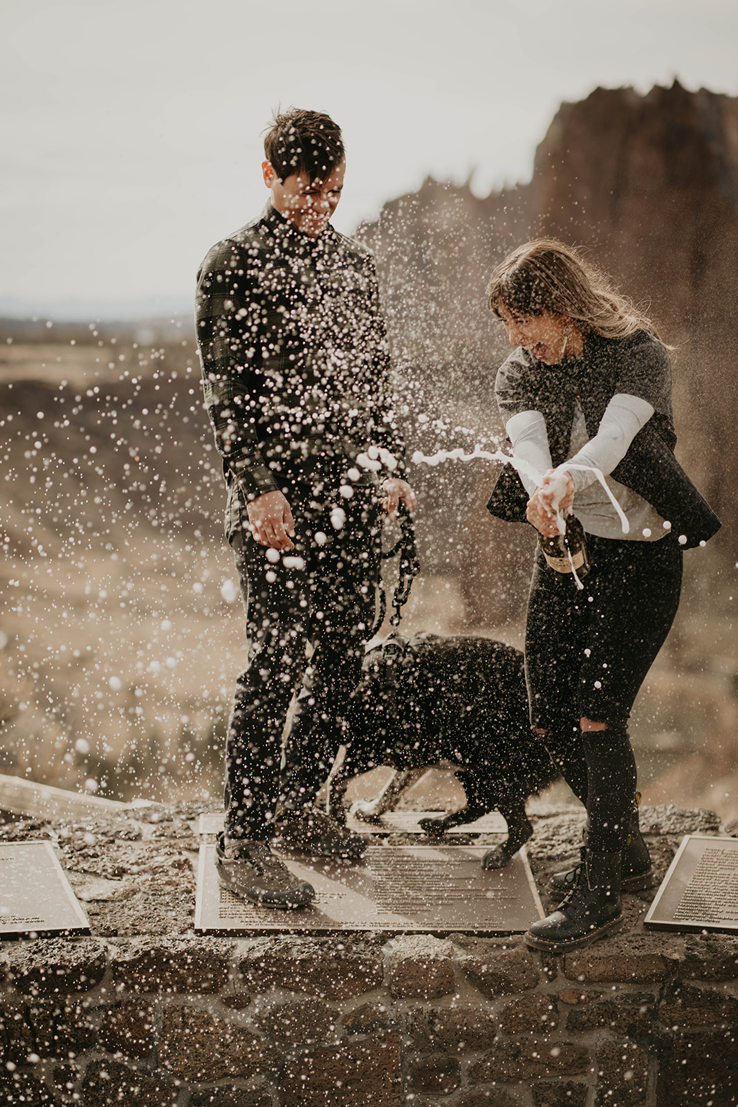 Couple popping champagne bottle at rock climbing engagement session