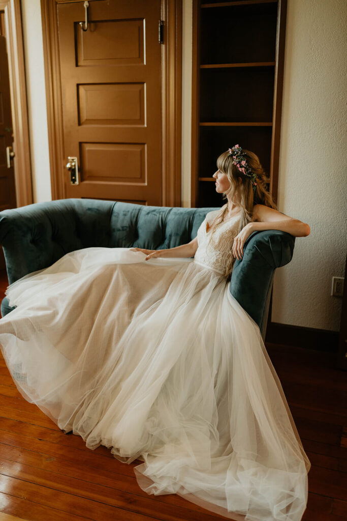 Bride sitting on blue velvet couch in white tulle wedding dress
