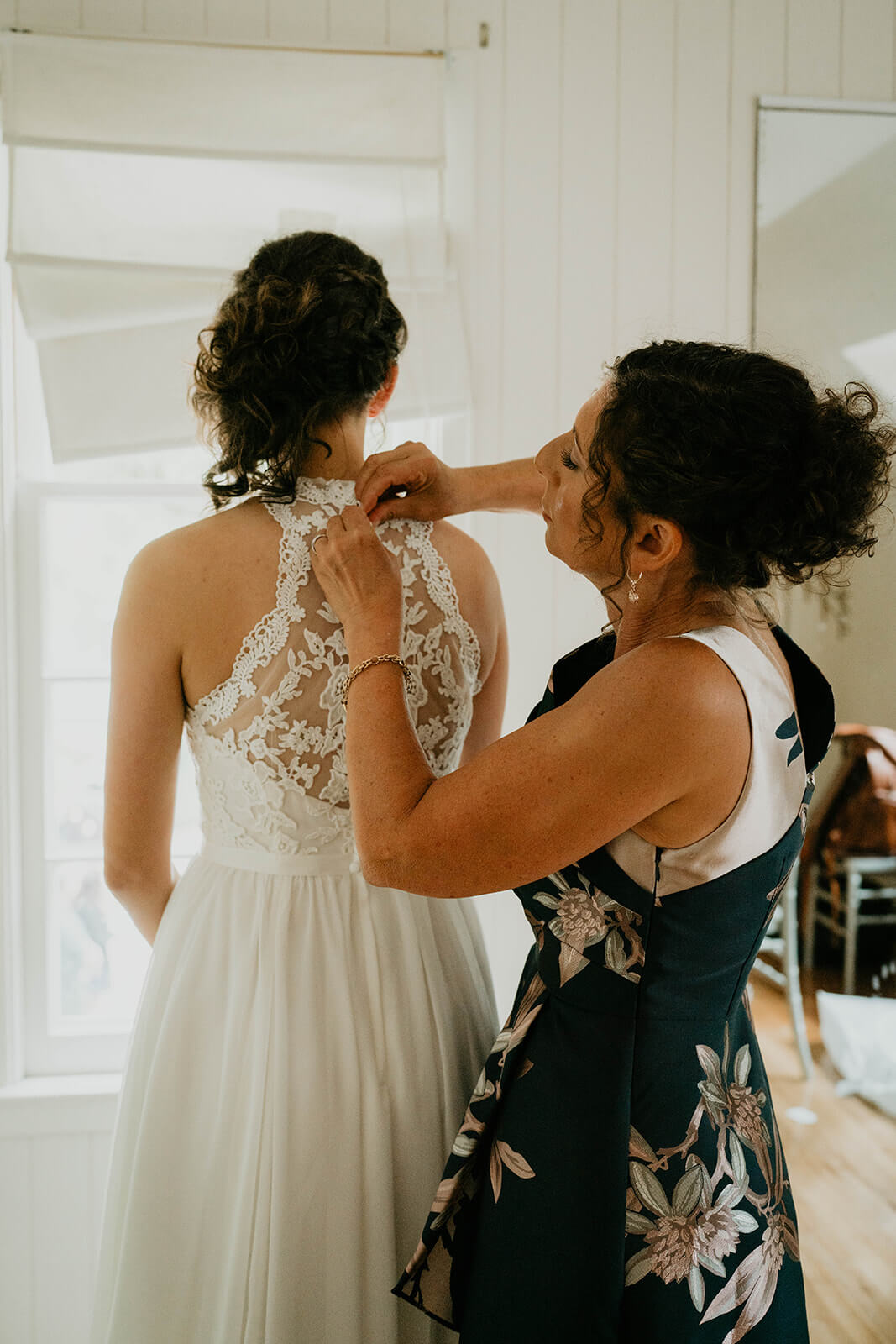 Mother of the bride helping bride into wedding dress