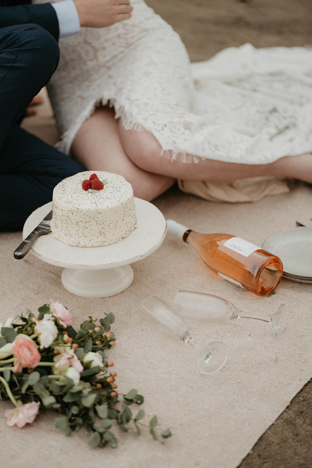 White wedding cake with rose bottle laying in the sand