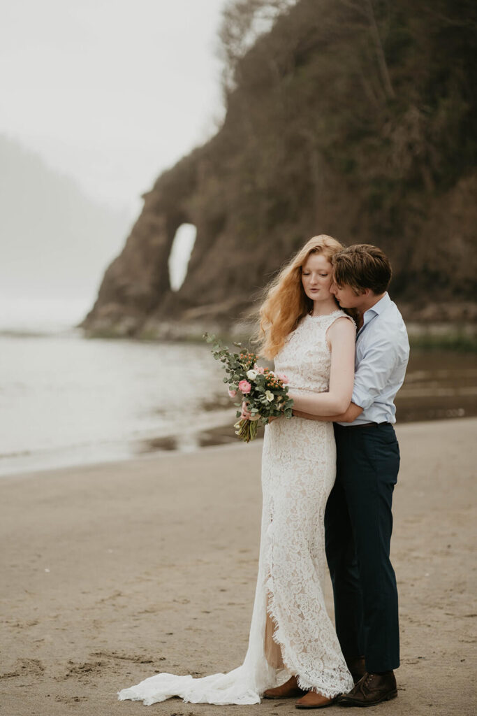 Groom hugs bride from behind during Oregon Coast elopement
