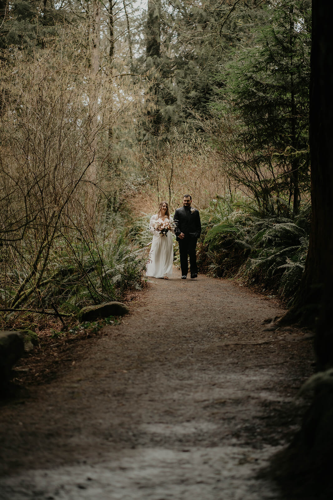 Bride and groom holding hands walking down a forest trail