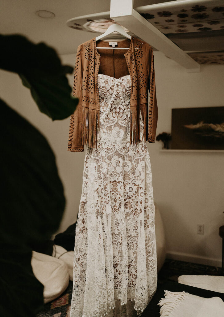 Lace wedding dress with suede fringe jacket hanging from hangar