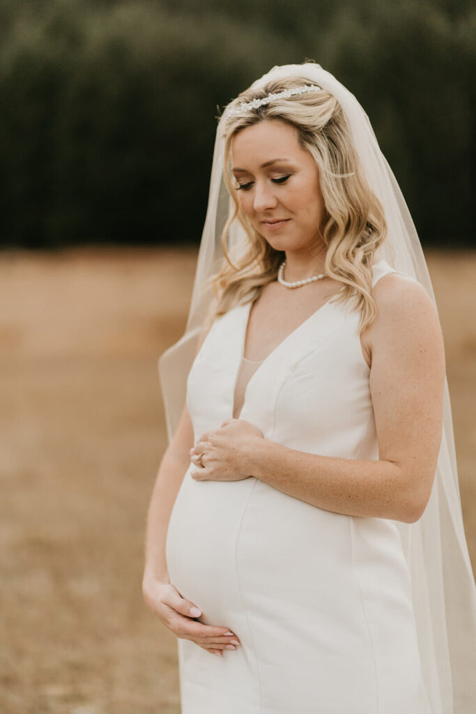 Bride holding pregnant belly during wedding portraits