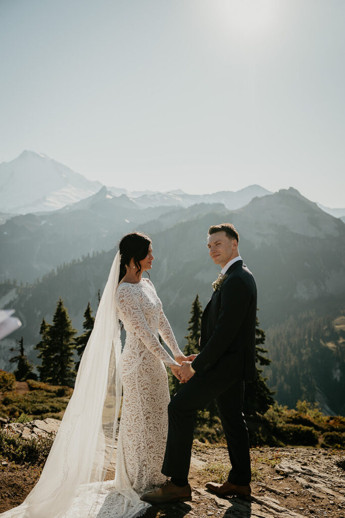 the bride and groom holding hands surrounded by mountains. 