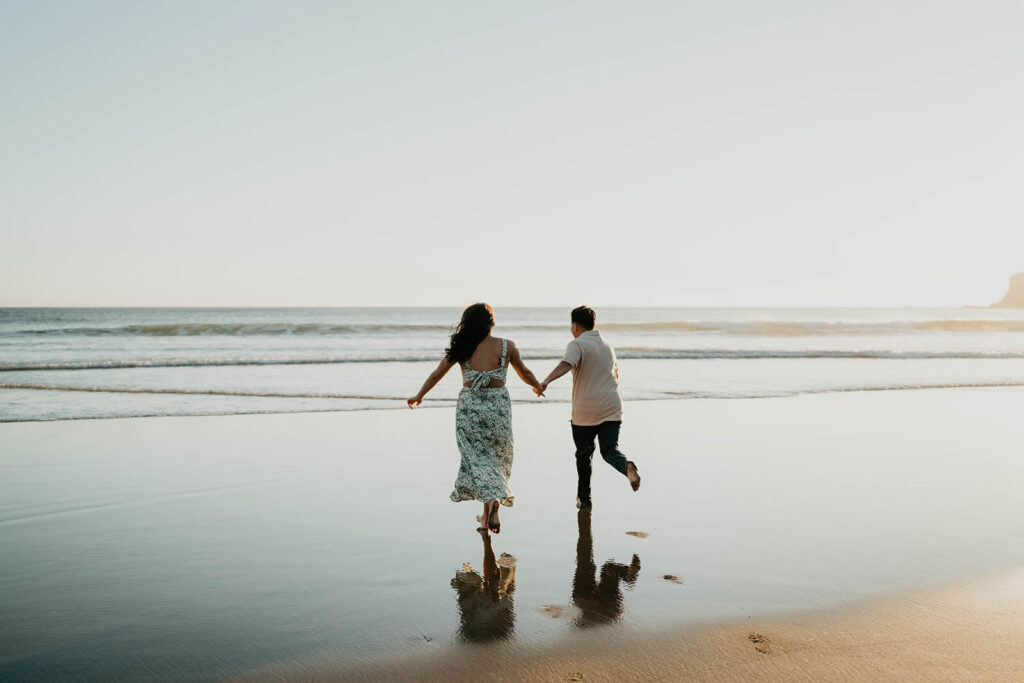 Couple holding hands running into the water on the Oregon Coast