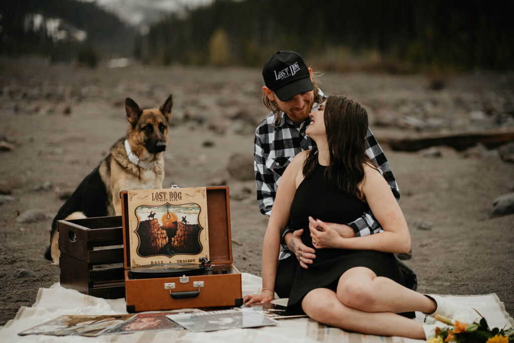 Couple sitting on white blanket with record player and german shepherd