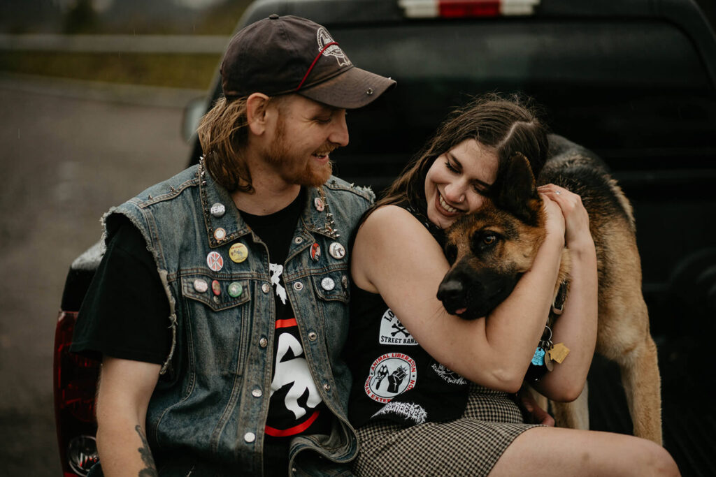 Couple sitting on the back of a truck while woman hugs german shepherd