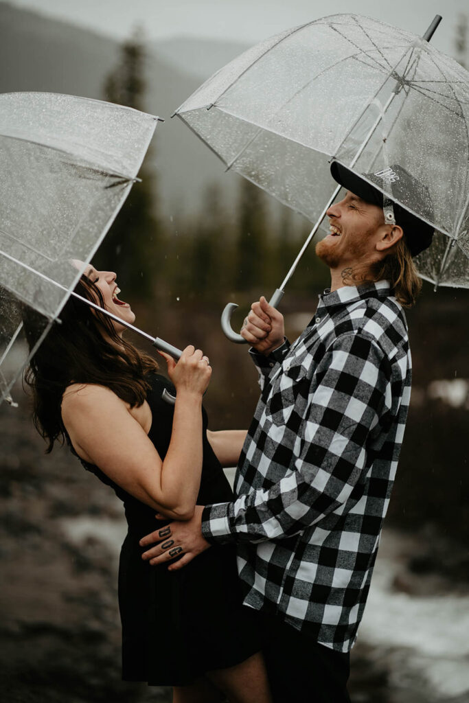 Couple holding clear umbrellas and laughing during Mt Hood engagement session