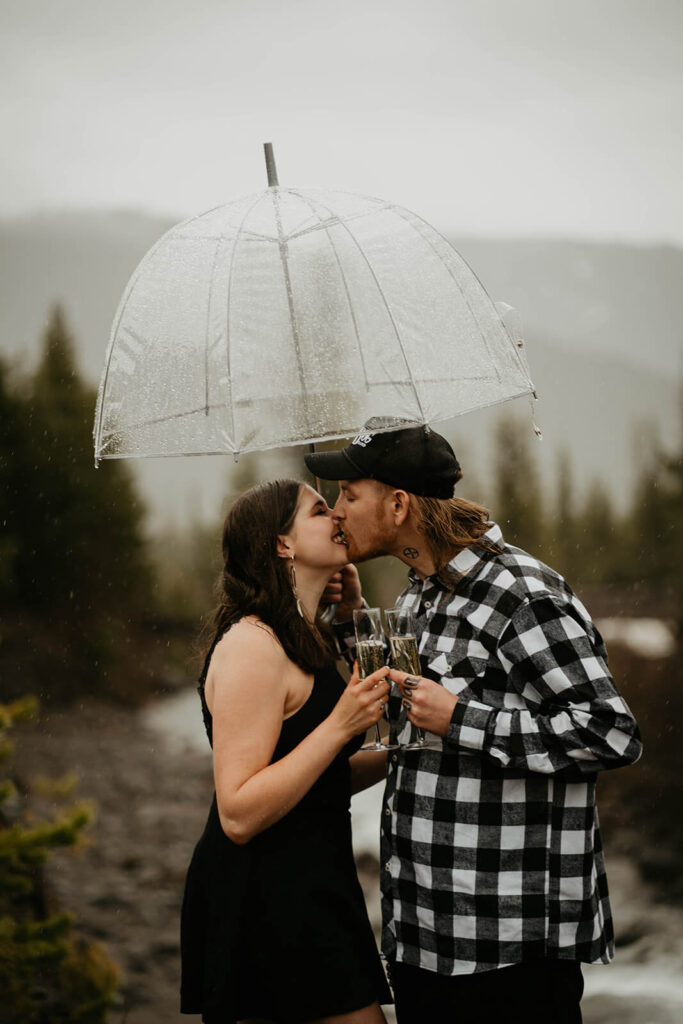 Couple holding champagne and kissing under a clear umbrella