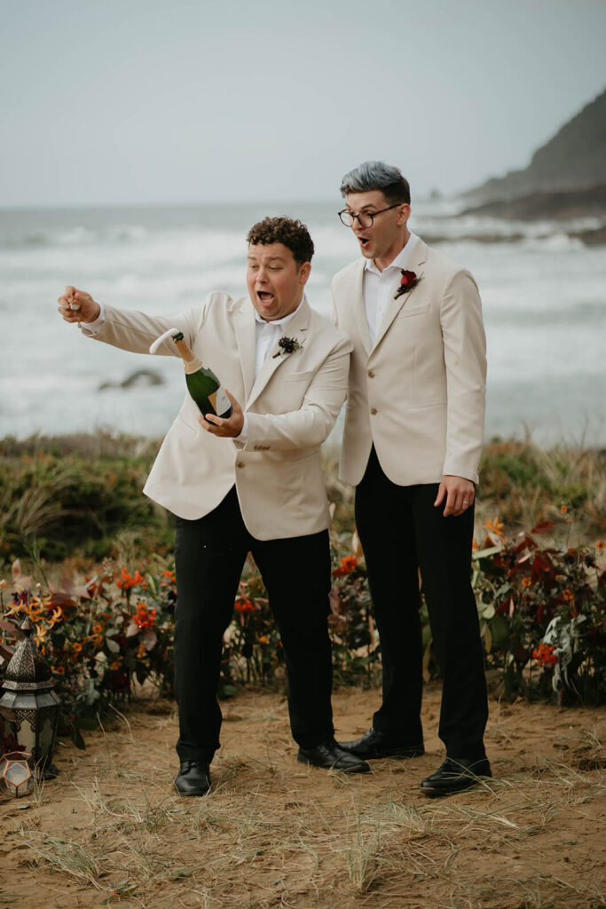 Grooms pop a bottle of champagne at their elopement on the rocky coast in Oregon