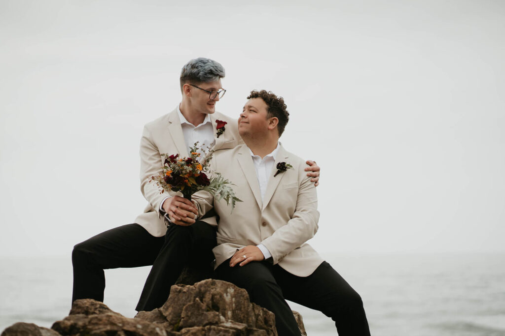 Two grooms sitting on a rock before their elopement ceremony on the Oregon Coast