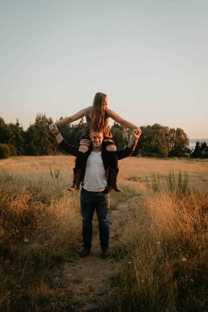Woman riding on man's shoulders during Seattle engagement photos at Discovery Park
