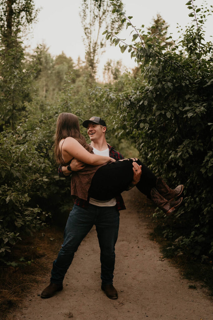 Man carrying woman during Seattle engagement photos at Discovery Park
