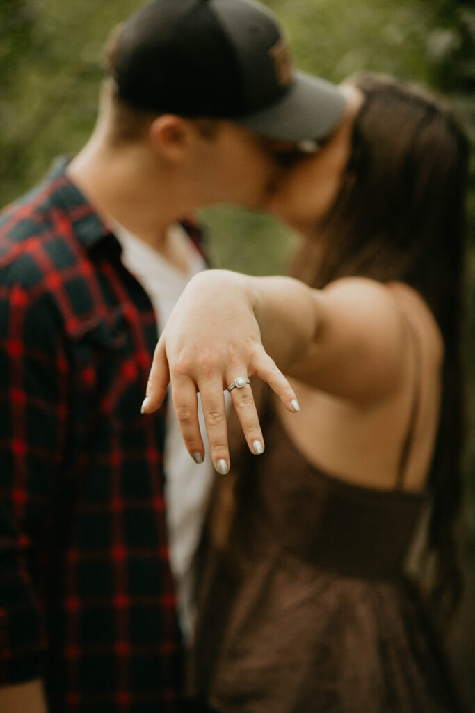 Woman holding out engagement ring while kissing her fiancee