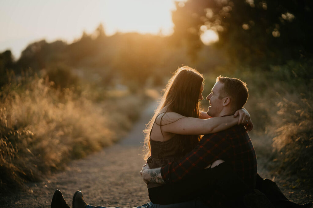 Couple sitting on the trail laughing and hugging during sunset engagement photos at Discovery Park