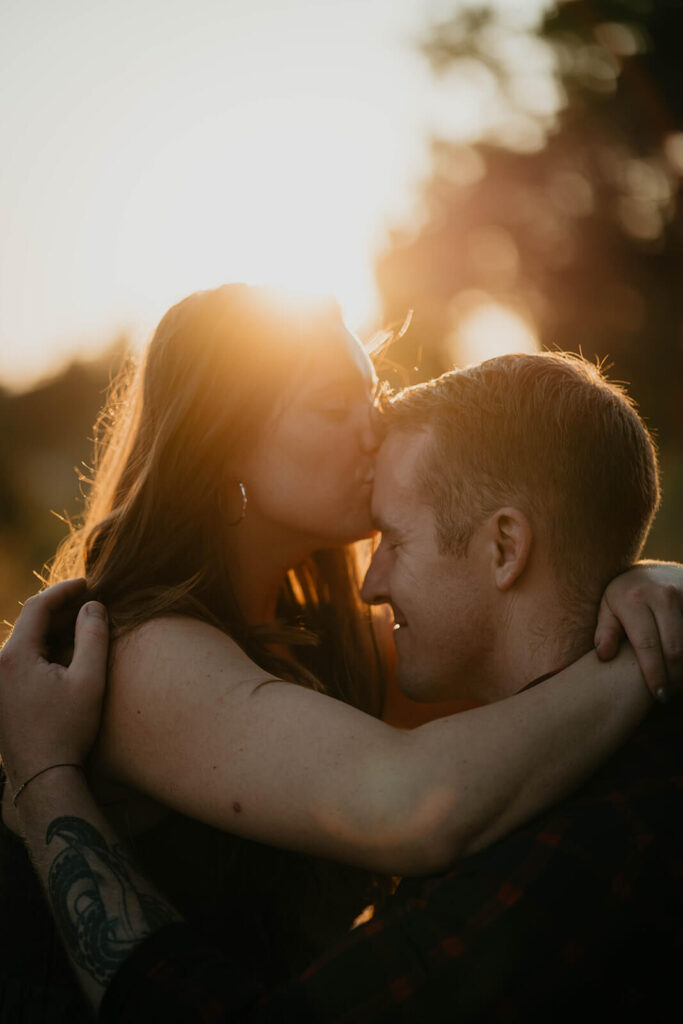 Couple sitting on the trail kissing during sunset engagement photos at Discovery Park