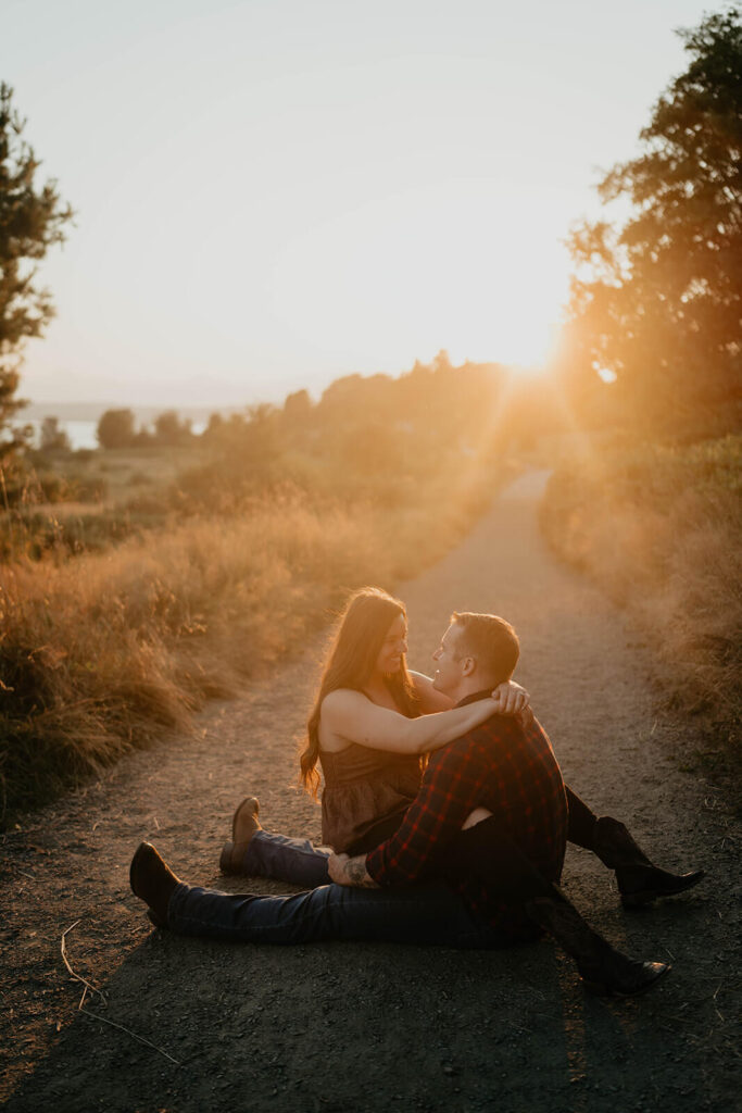 Couple sitting on the trail hugging during sunset engagement photos at Discovery Park