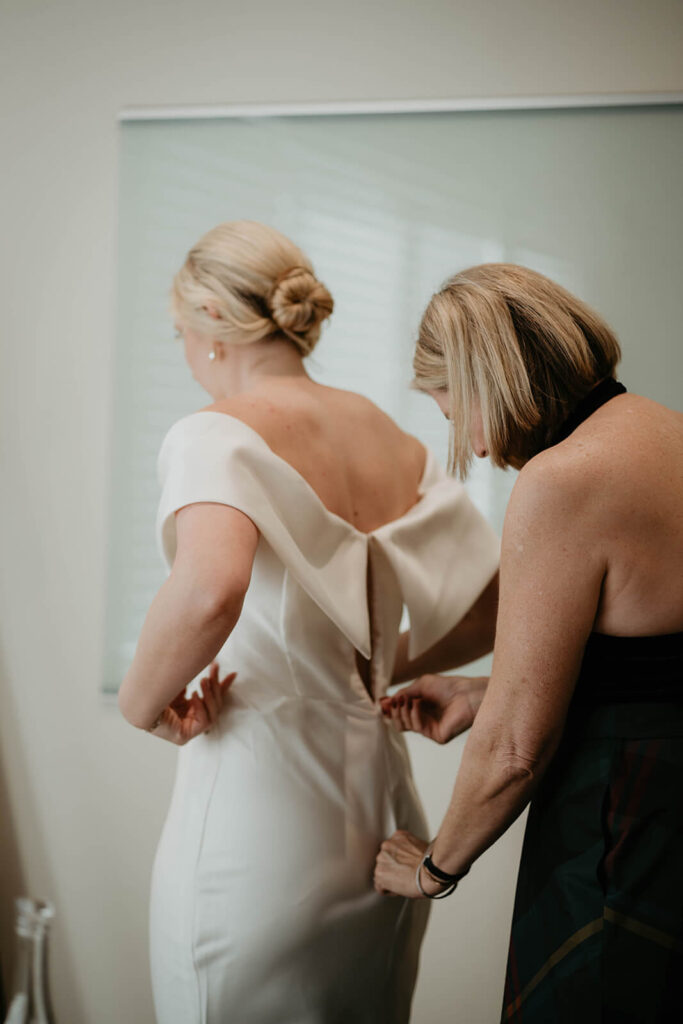 Bride's mother helping zip her into her wedding dress at vineyard wedding