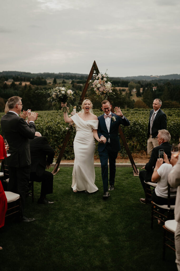 Bride and groom cheer as they exit the wedding aisle at vineyard wedding