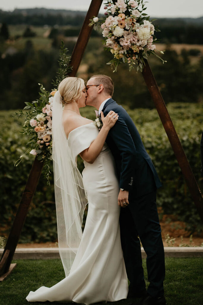 Bride and groom kiss during outdoor wedding ceremony at Ponzi Vineyards