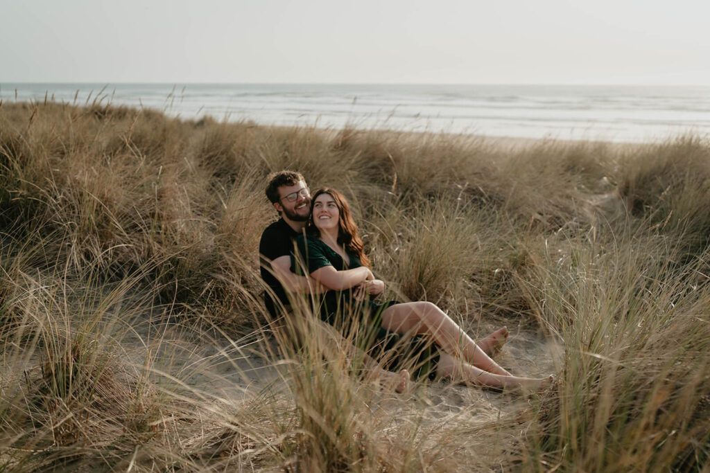 Couple sitting in the grass during their engagement photos on the beach