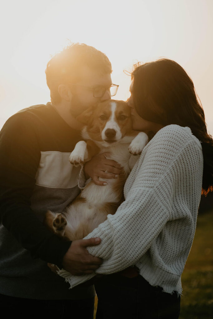 Couple kissing their dog during engagement photo session on the beach