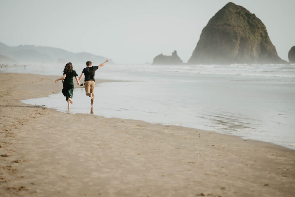 Couple running in the sand for engagement photos on the beach