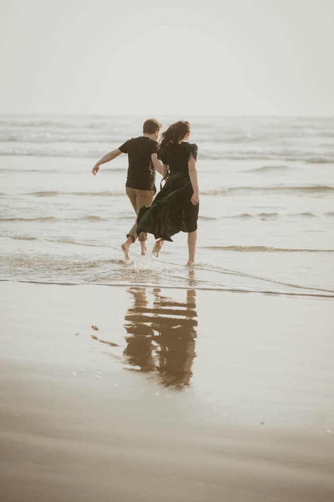 Couple holding hands, running across Cannon Beach during their beach engagement photos