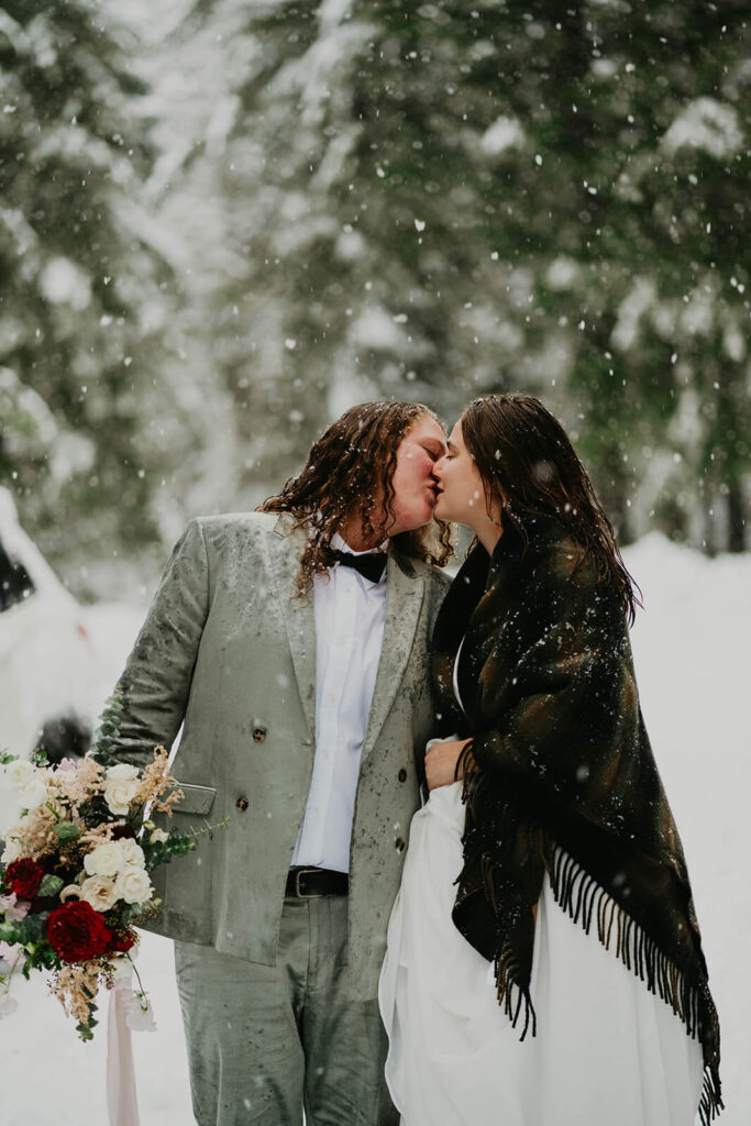 Brides kissing in the snow at winter wonderland cabin elopement