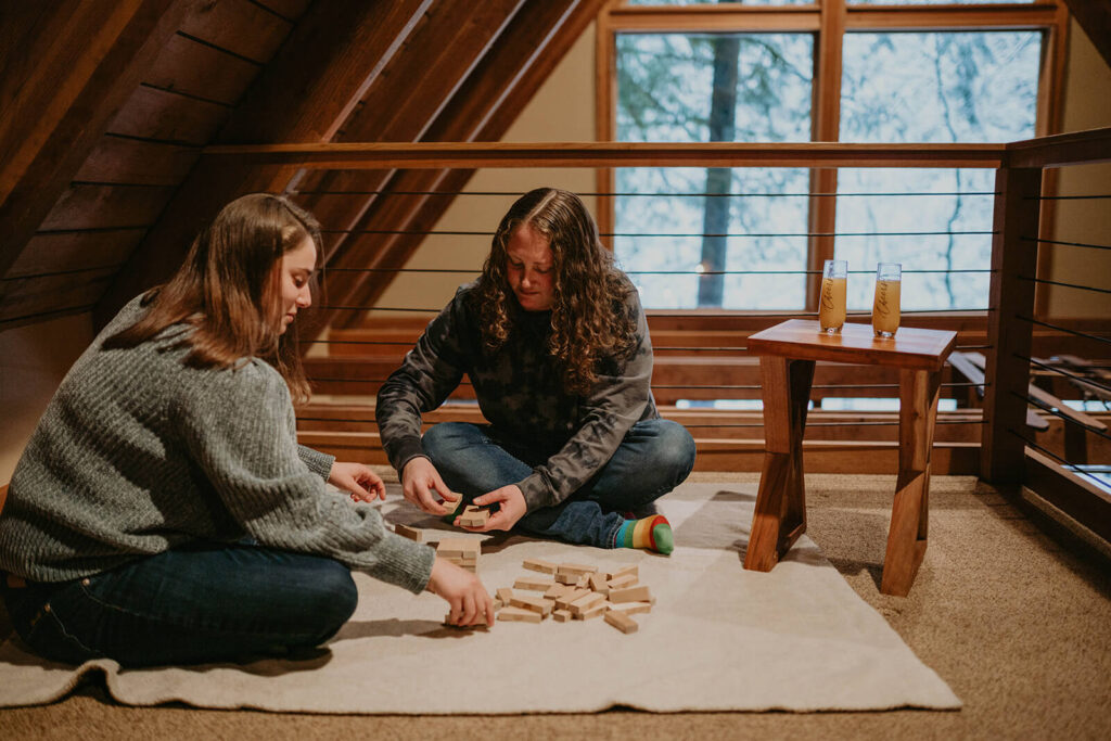 Two women sitting on the floor of their winter wonderland cabin playing Jenga