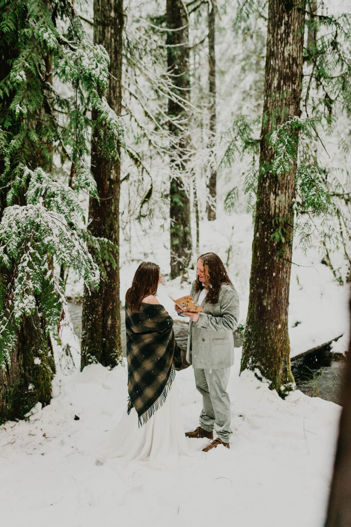 Two brides exchanging vows in the forest during winter wonderland cabin elopement