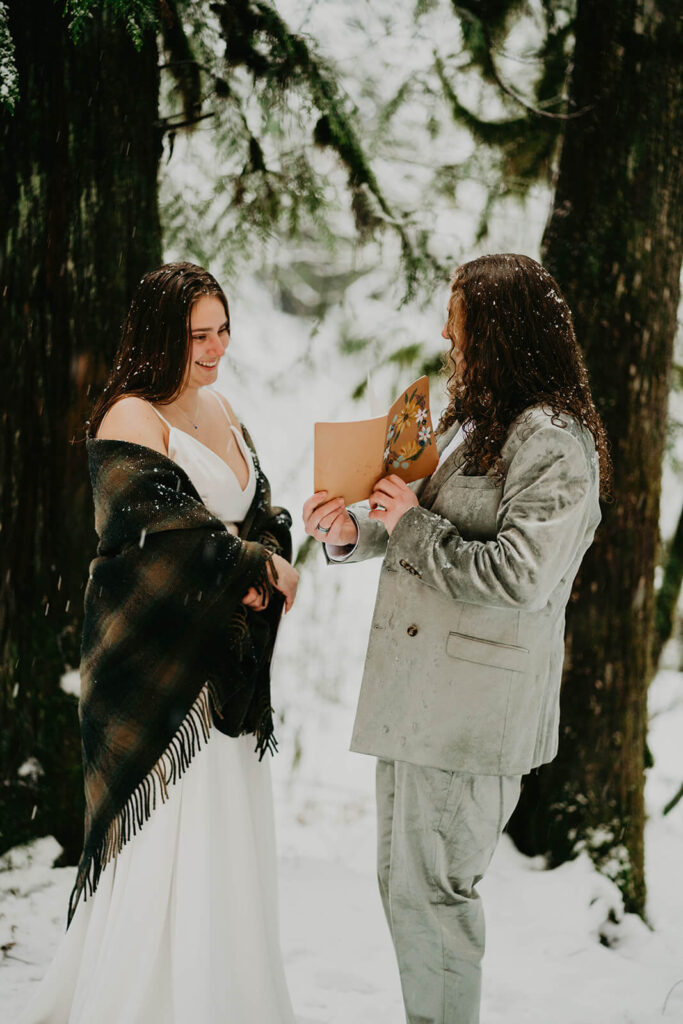 Two brides exchanging vows in the snow at winter wonderland cabin elopement in Oregon