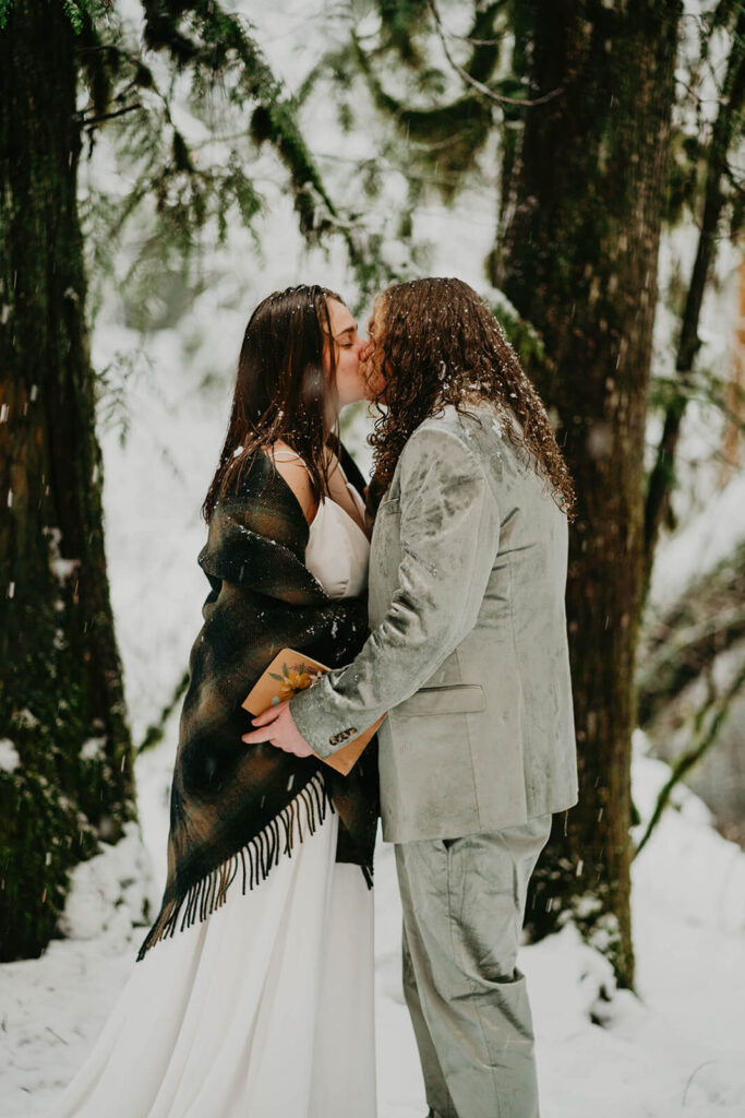 Two brides kissing in the snow at cozy Christmas cabin elopement in Oregon