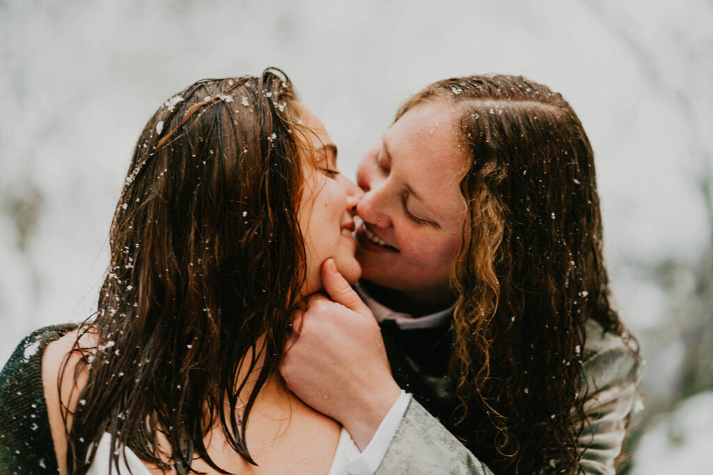 Two brides kissing in the snow at cozy Christmas cabin elopement in Oregon
