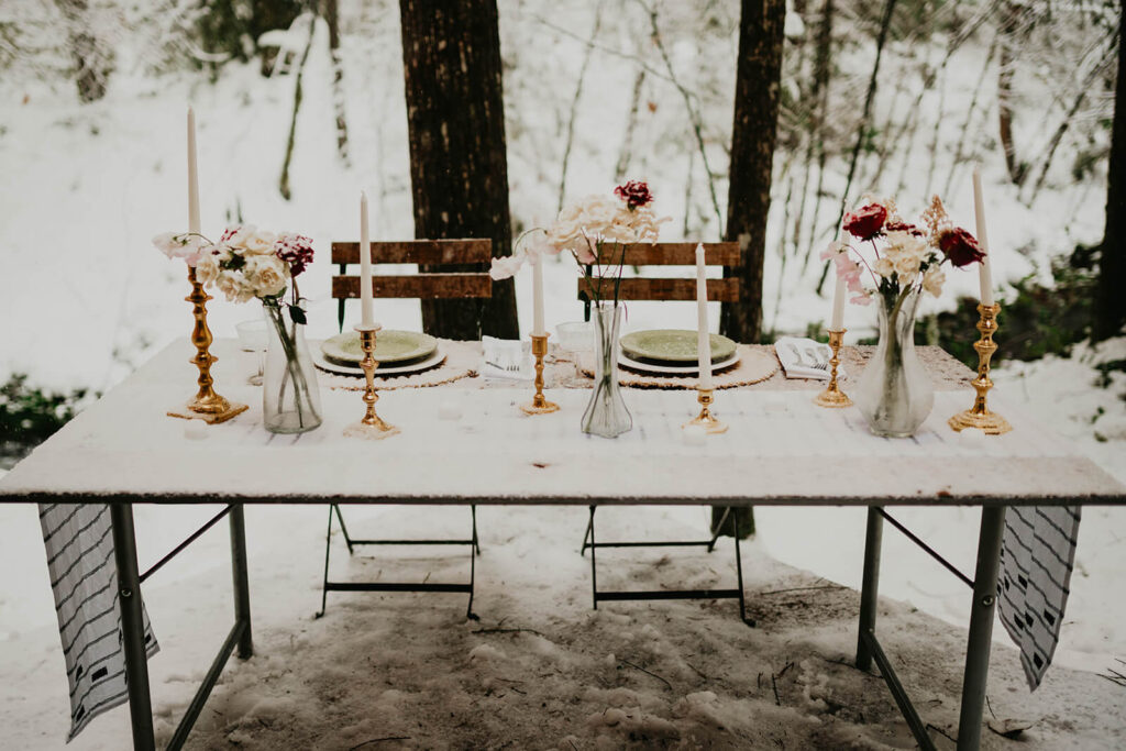 White, burgundy, and gold sweetheart table in the snow at cozy Christmas cabin elopement