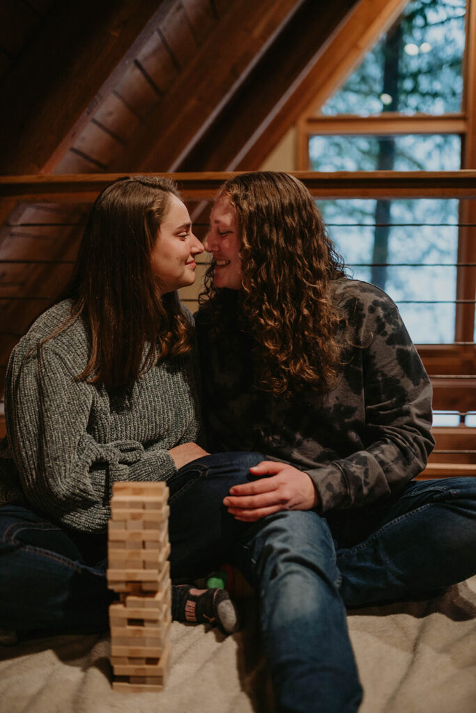 Two women sitting on the floor kissing while playing Jenga in their winter wonderland cabin