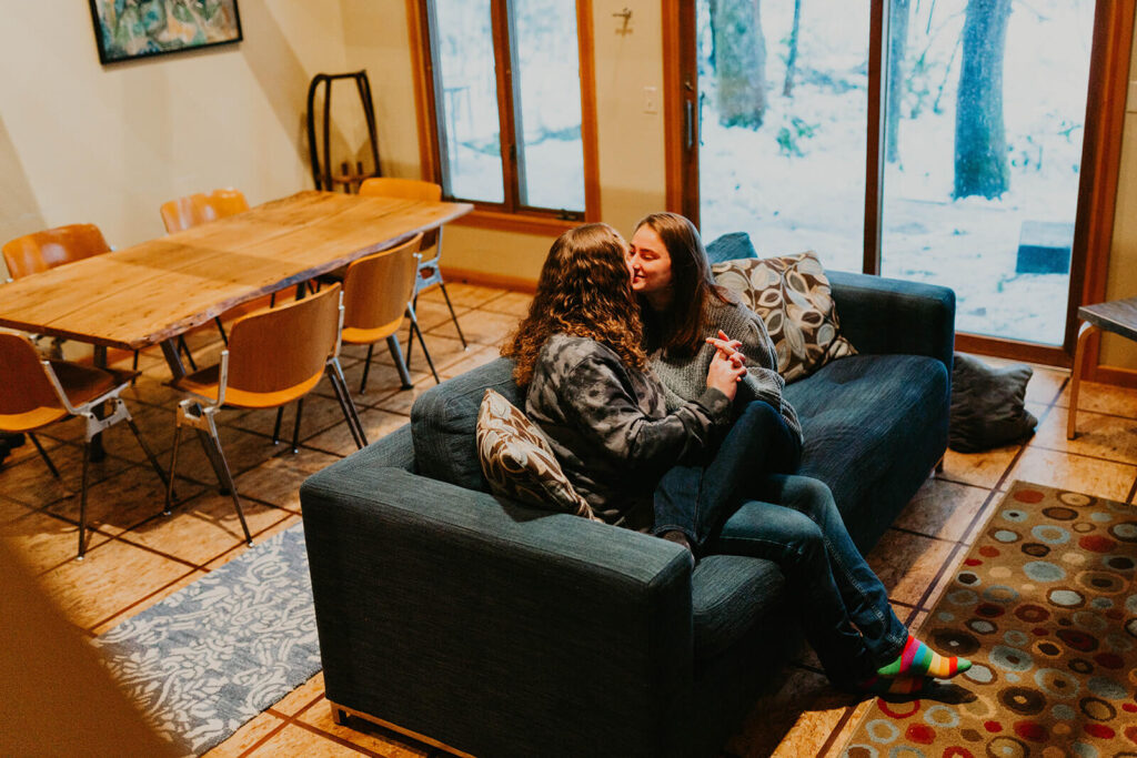 Two women sitting on a blue couch kissing during their winter wonderland cabin elopement in Oregon
