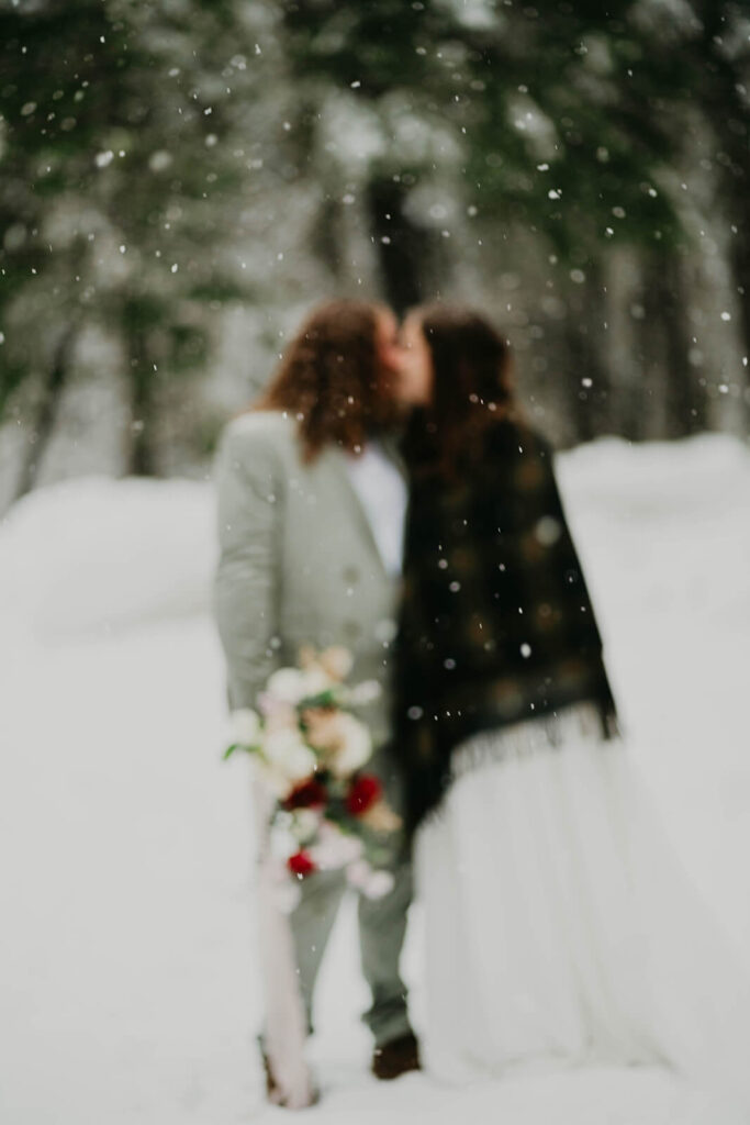 Two brides kissing in the snow at cozy Christmas cabin elopement at Mt Hood