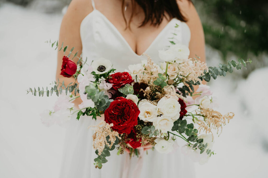Bride holding white, red, and green floral bouquet at winter wonderland cabin elopement