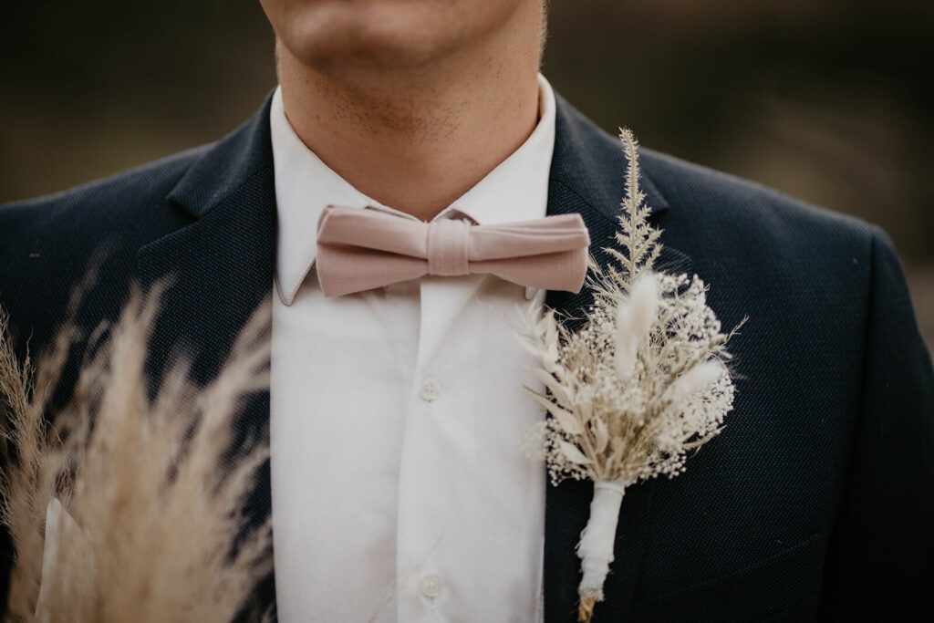 Groom in navy suit with light pink bow tie and dried floral boutonniere 