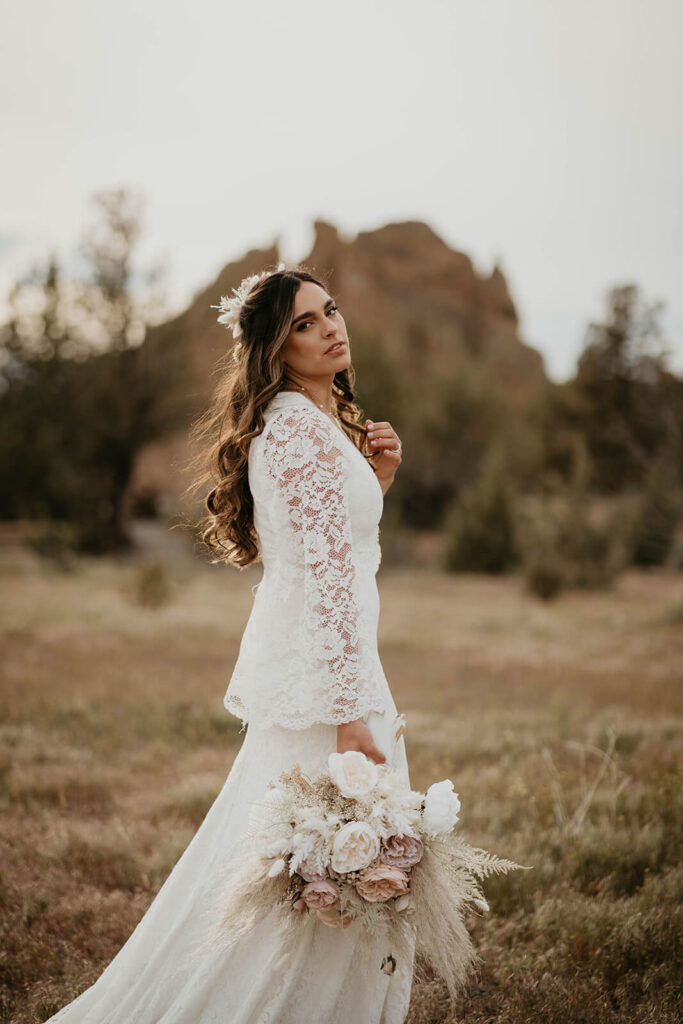 Bride in white lace boho wedding dress holding a bouquet of neutral flowers