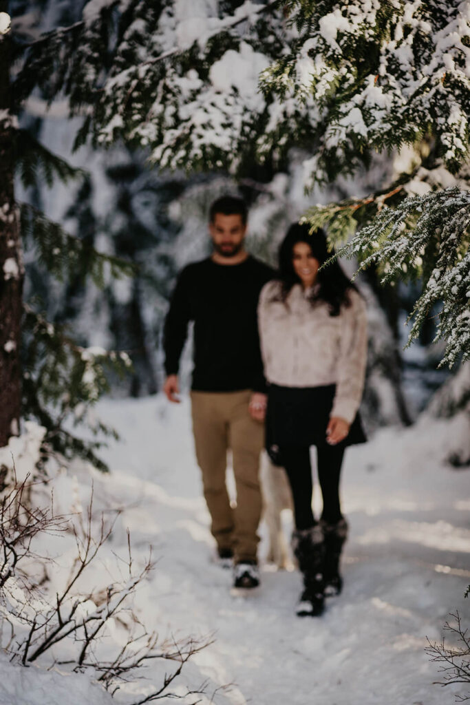 Couple holding hands walking through the snow during winter engagement photo session