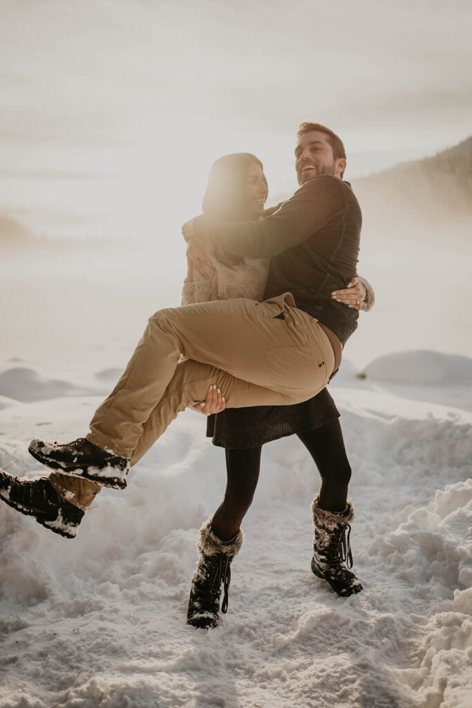 Woman picking up man during snow engagement photos 