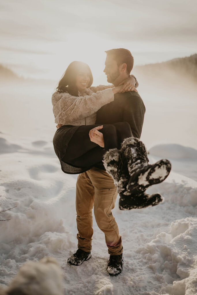 Man picking up woman during snow engagement photos