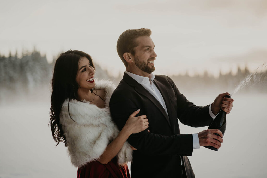 Couple popping champagne during engagement photos in the snow